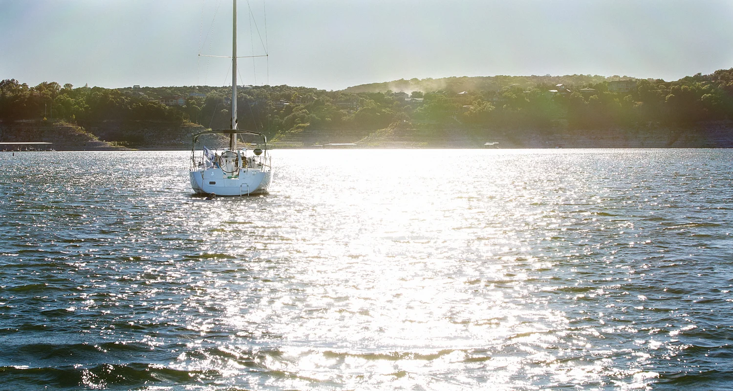 Sailboat on Lake Travis with sunlight on the water and limestone hills